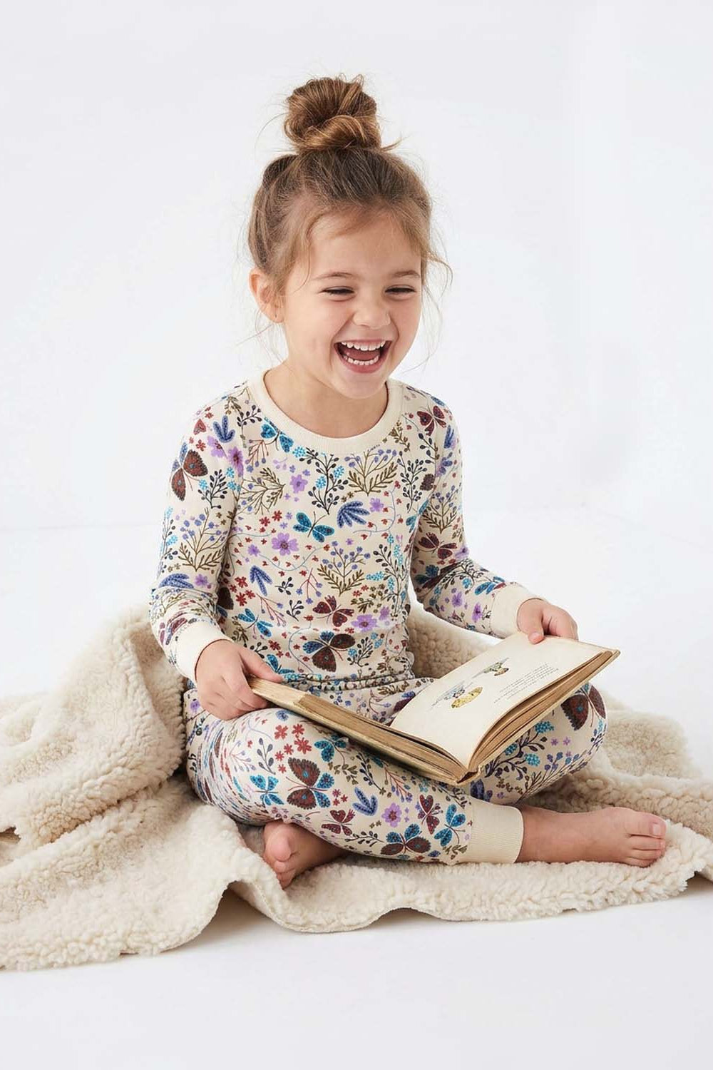 Child in floral pajamas reading a book on a white background