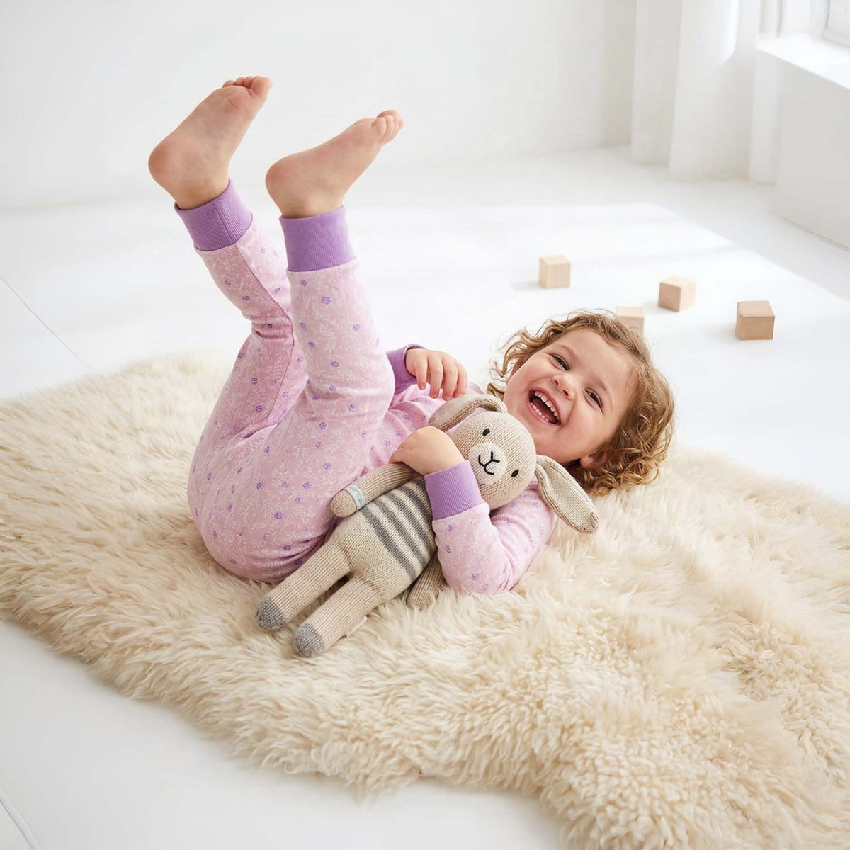 Child in pink pajamas with a plush toy on a fluffy rug