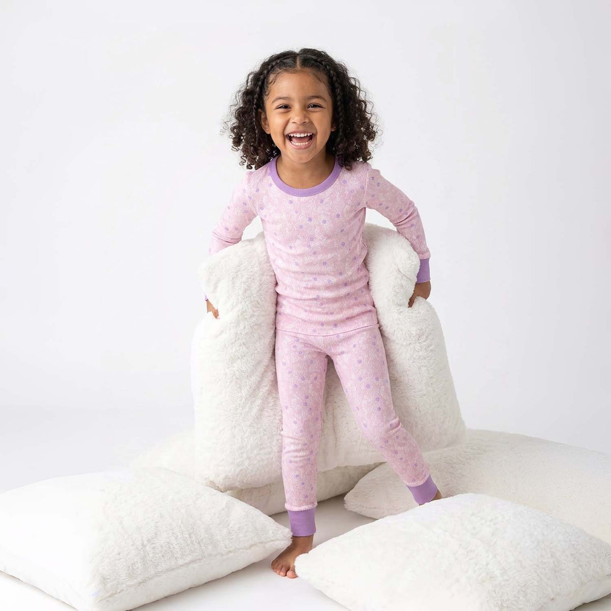 Child wearing pink pajamas with a white pillow background