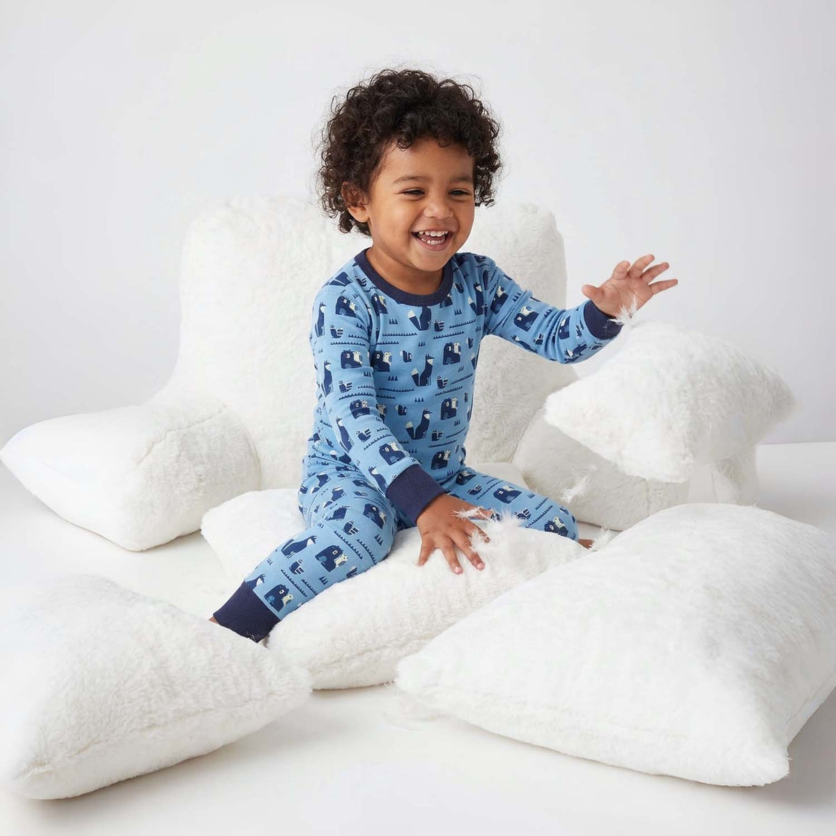 Child wearing blue pajamas with animal pattern sitting on white pillows.