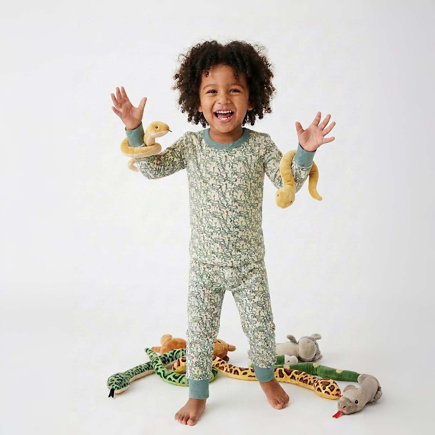Child wearing a green snake pajamas with toys on a white background