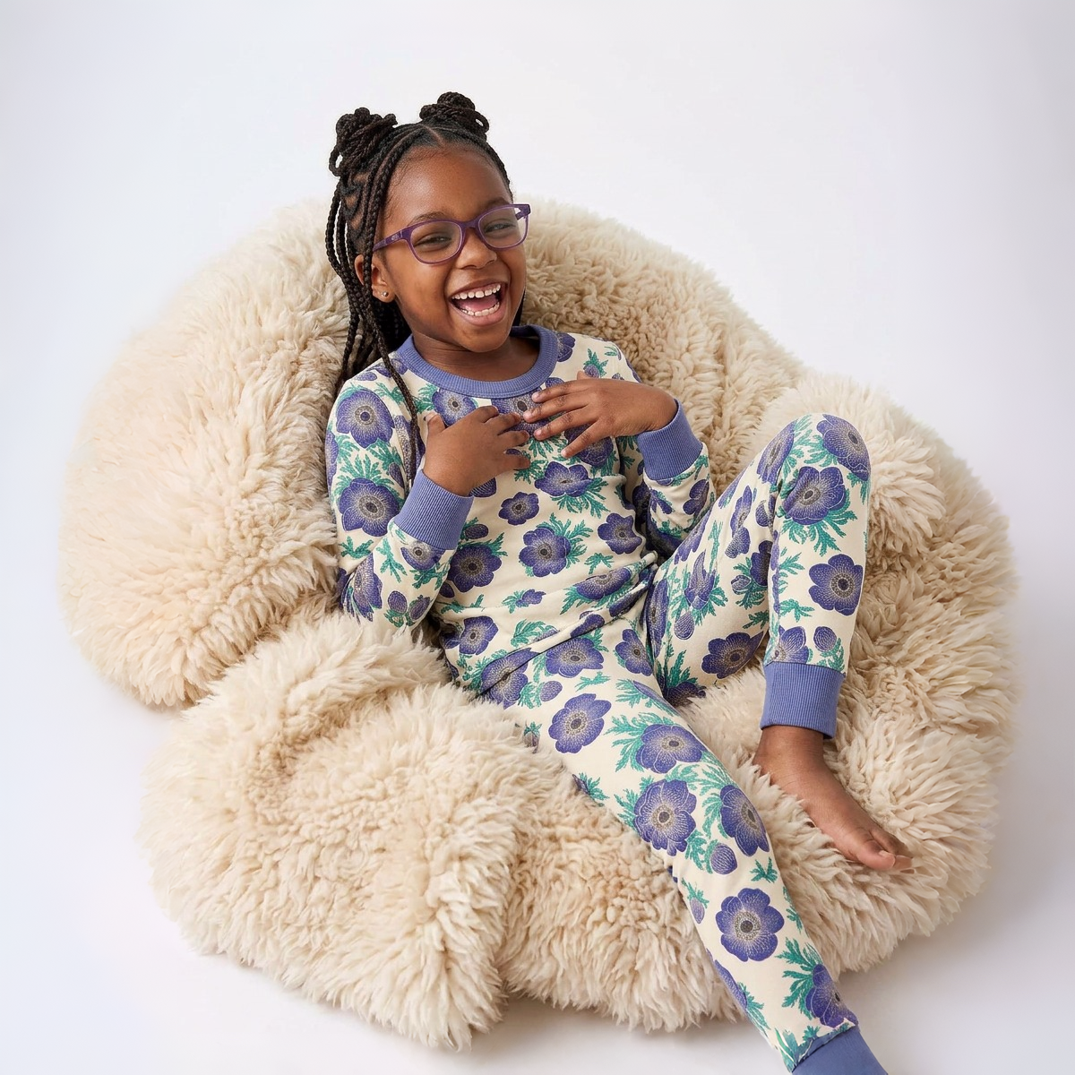 Child wearing a floral pajama set sitting on a fluffy chair.