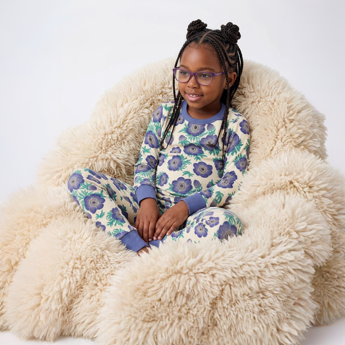Young girl wearing a floral pajama set sitting on a fluffy chair.
