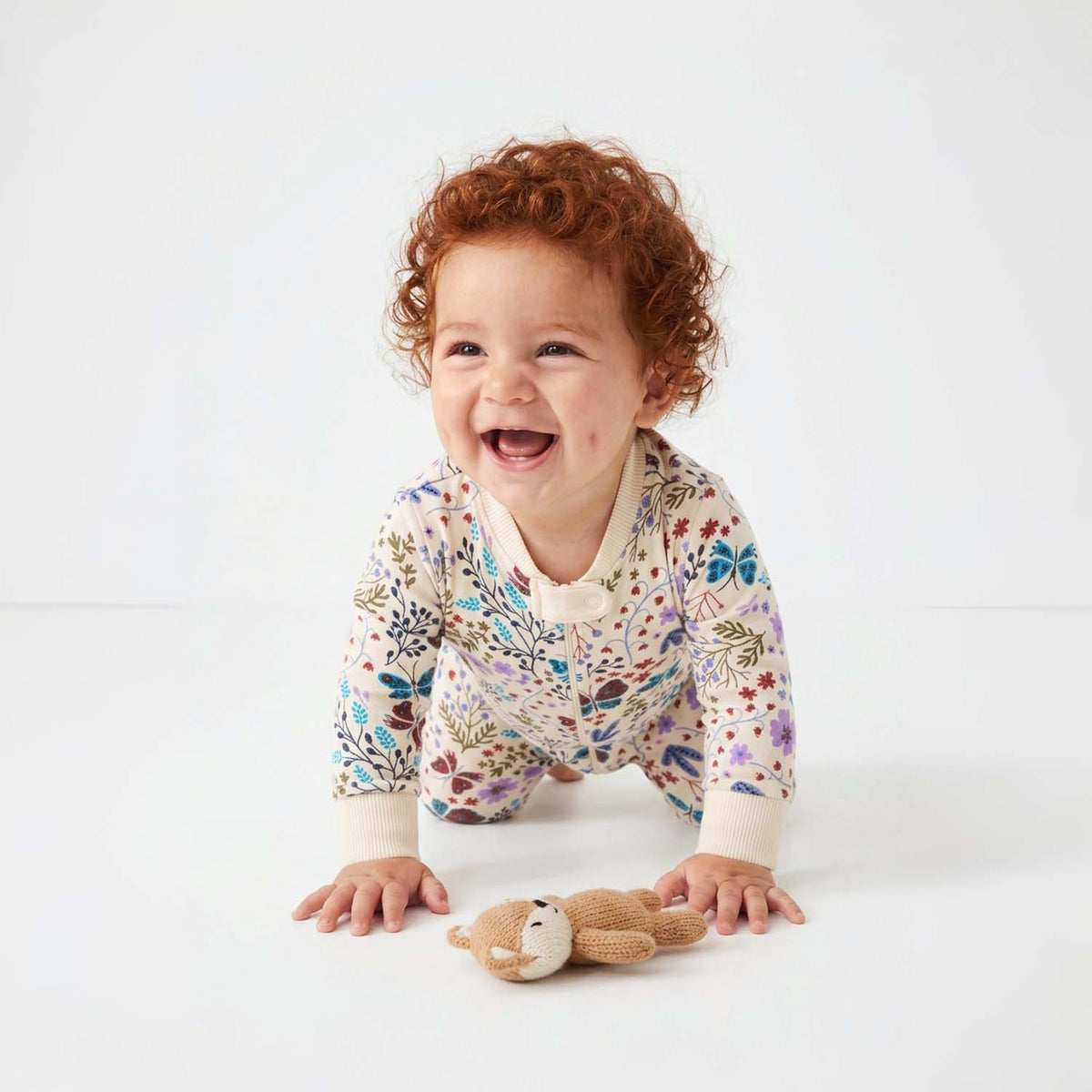 Baby in a floral onesie with a toy on a white background