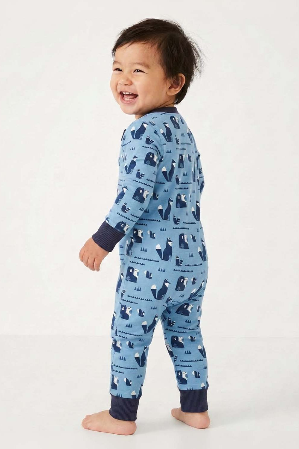 Baby standing wearing a blue pajama with animal pattern on a white background