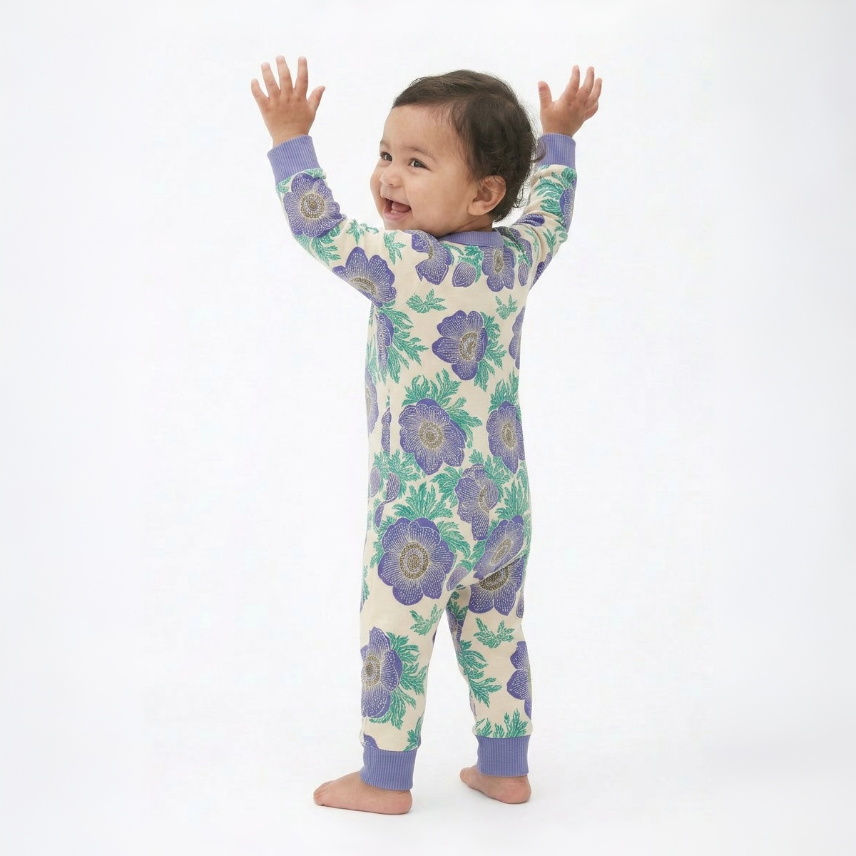 Baby wearing a floral onesie with arms raised on a white background