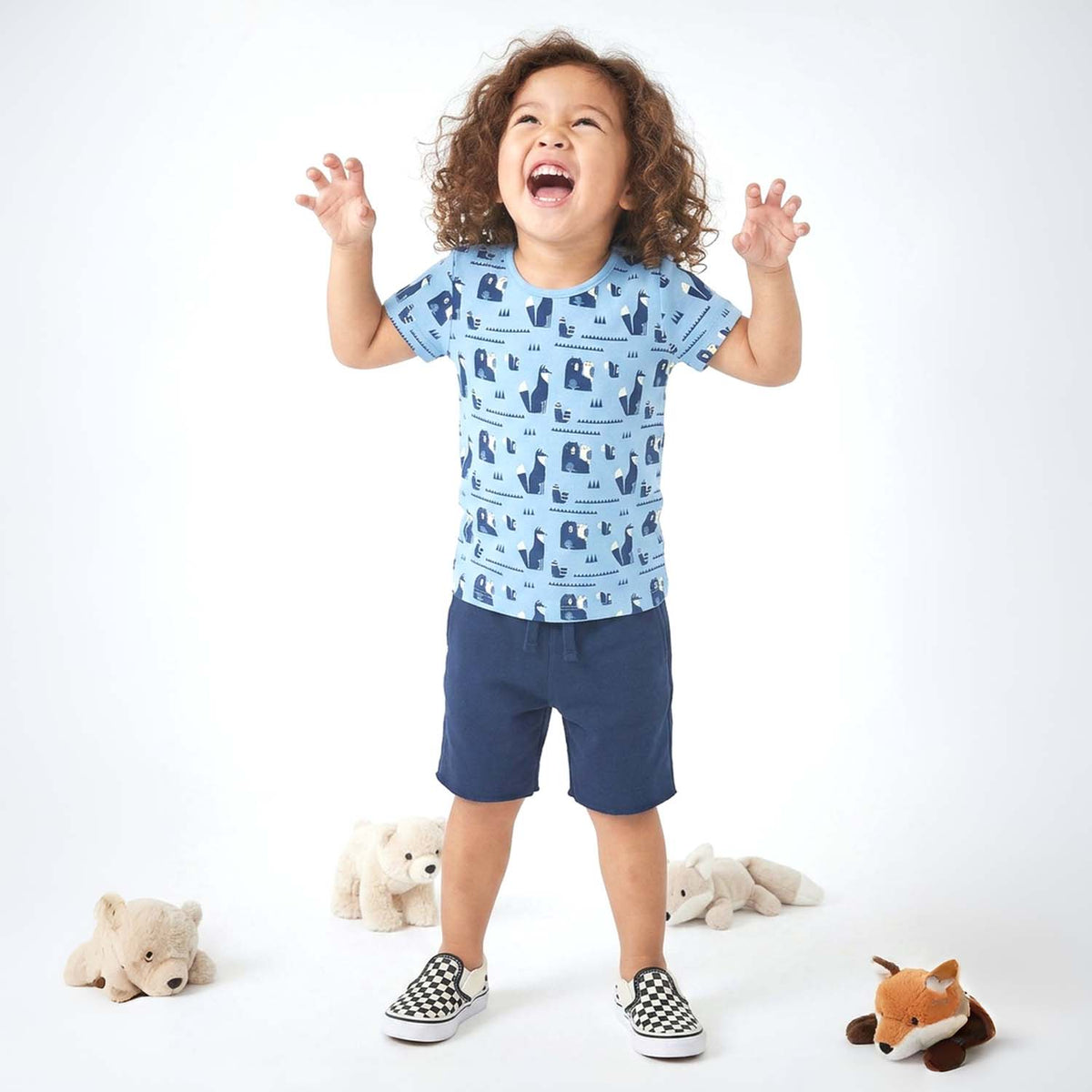 Child wearing a blue patterned shirt and navy shorts with teddy bears in the background