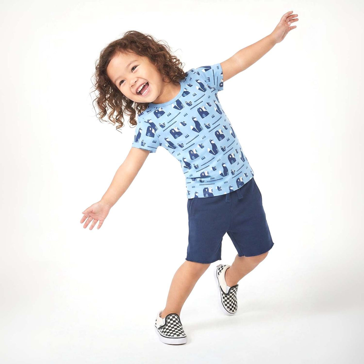 Child wearing a blue patterned shirt and navy shorts on a white background