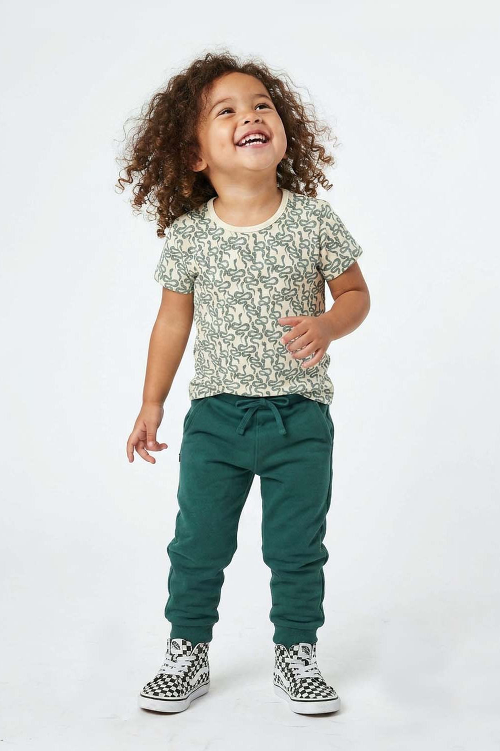 Child wearing a snake patterned shirt and green pants on a white background