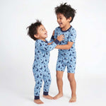 Two children wearing blue pajamas with a pattern, standing on a white background