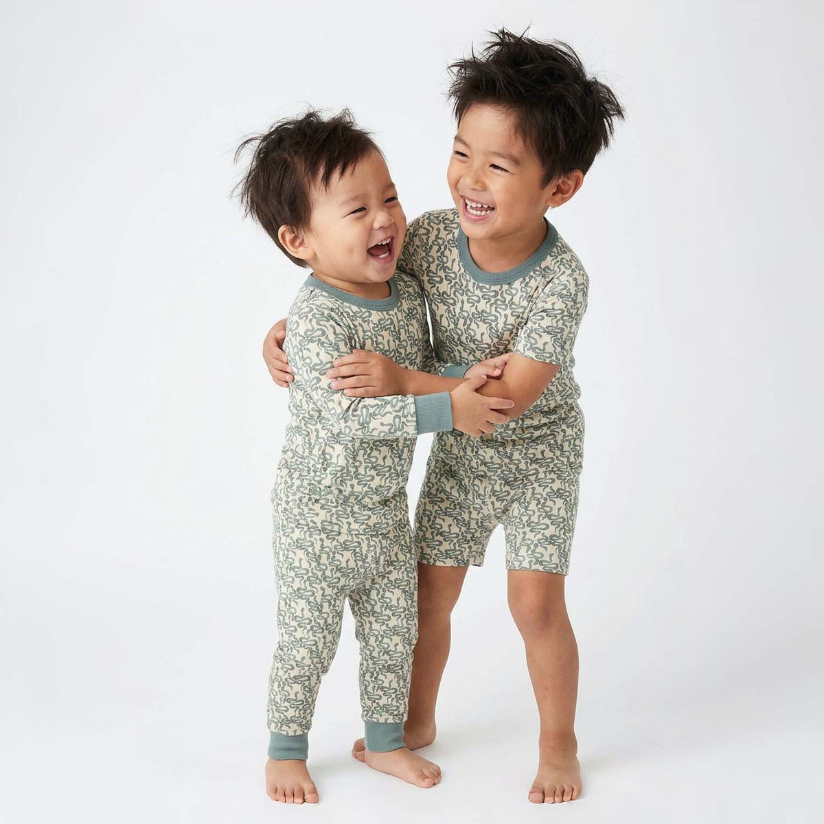 Two children wearing matching green snake pattern pajamas on a white background