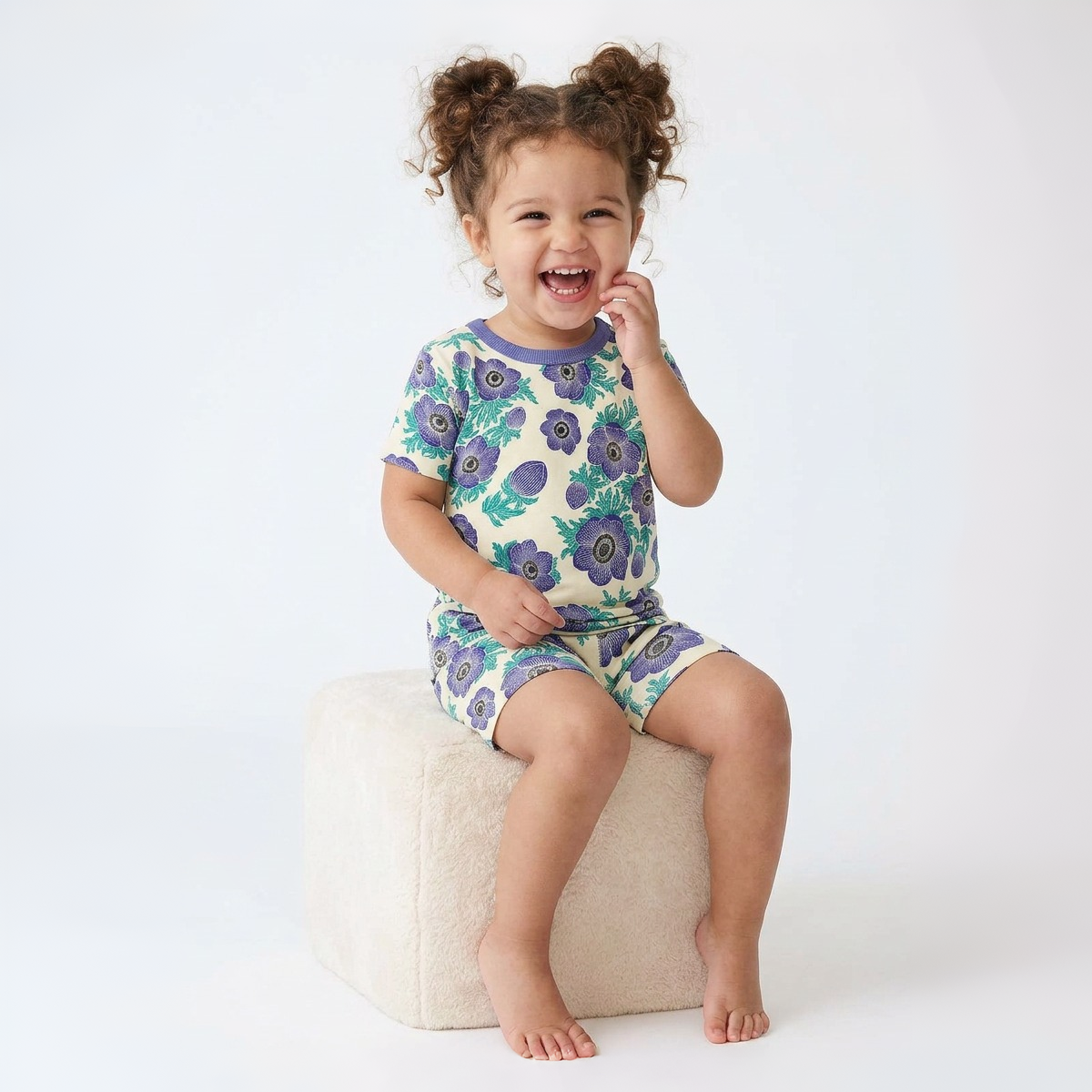 Child wearing a floral pajama set sitting on a white stool against a white background