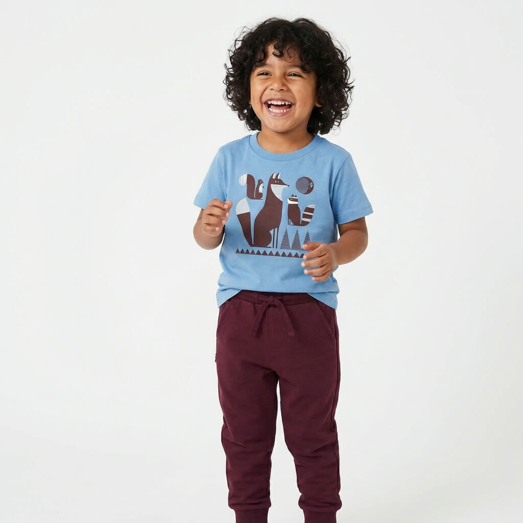 Young child with black hair wearing a Mightly 100% organic cotton graphic tee with a colorful fox print and burgundy sweatpants.