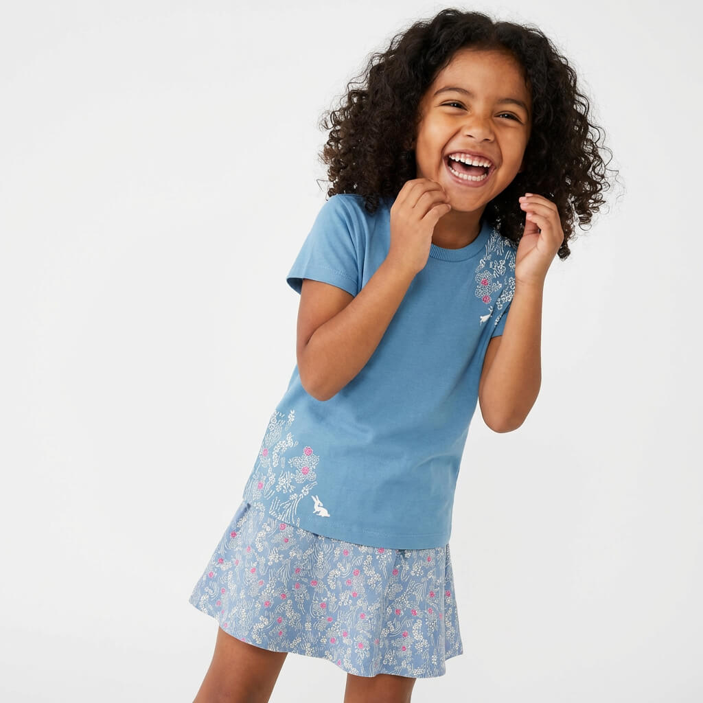 Young girl wearing a Mightly 100% organic cotton graphic tee with a pink and white print featuring flowers and bunnies and a matching skirt.