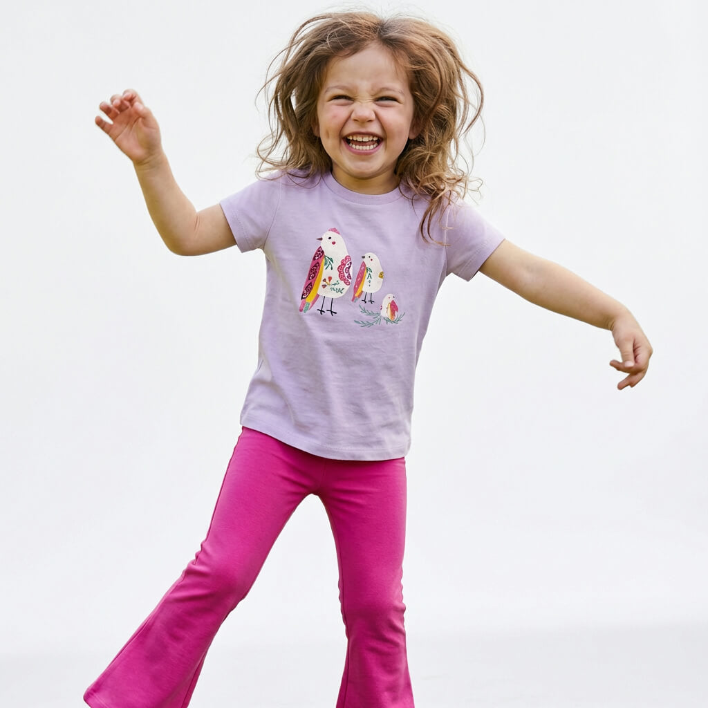 Young girl wearing a Mightly 100% organic cotton graphic tee with a colorful bird print and bright pink pants.