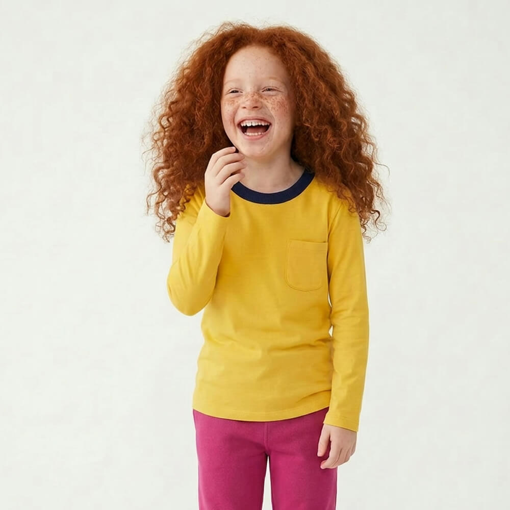 Child wearing a yellow long-sleeve shirt with a pocket and pink pants on a white background