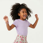 Child wearing a purple shirt and floral skirt on a white background