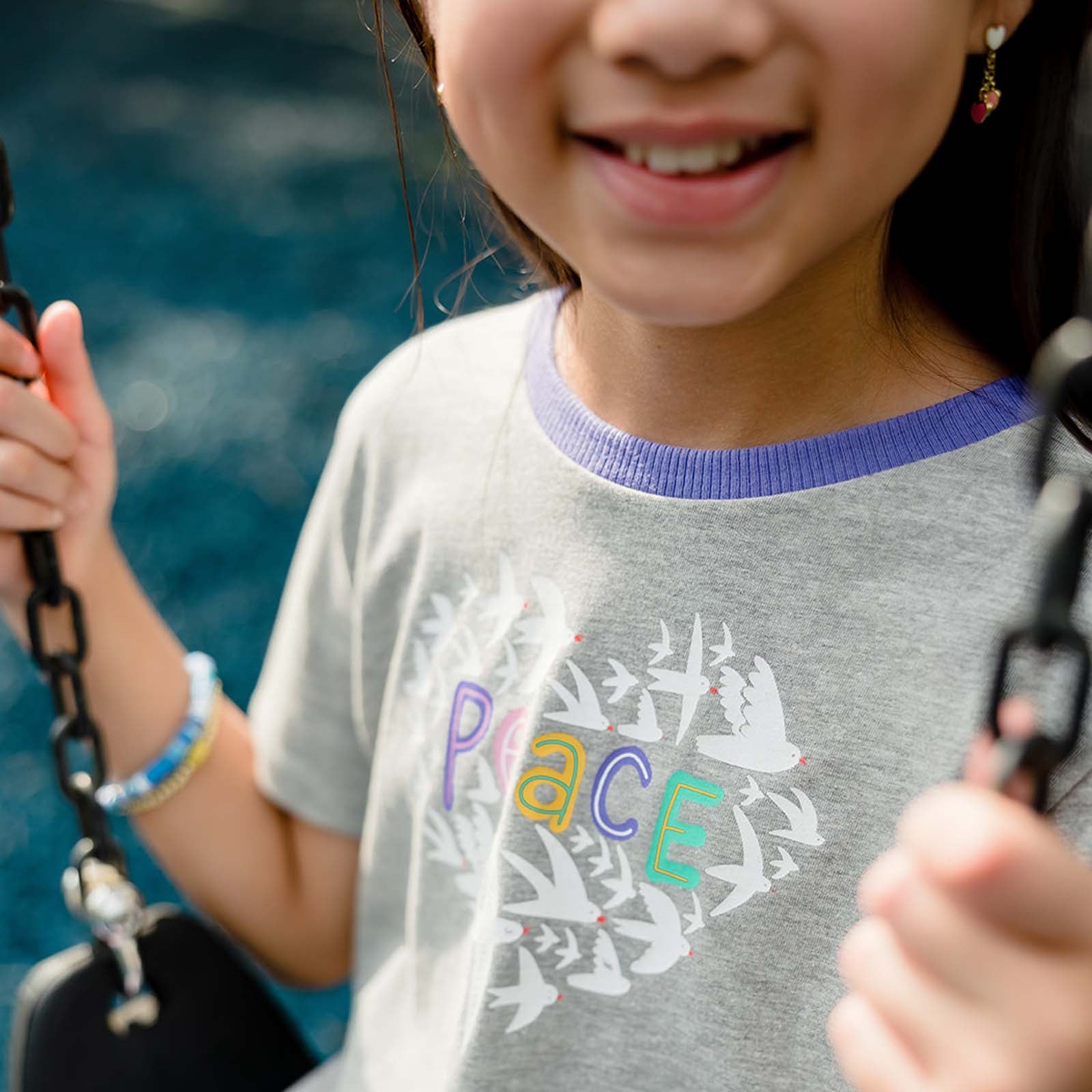 Child wearing a gray t-shirt with 'PEACE' printed on it, holding onto something with a blurred background.