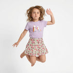 Child wearing a purple t-shirt with a colorful design and a floral skirt on a white background
