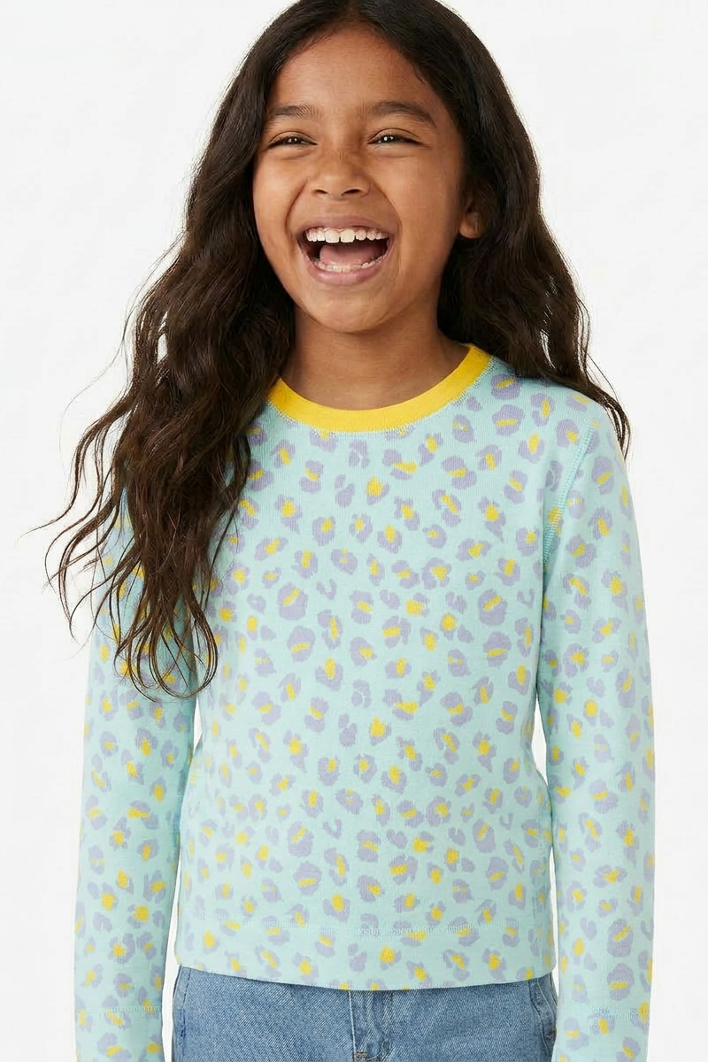 Young girl wearing a light blue long-sleeve shirt with a floral pattern on a white background