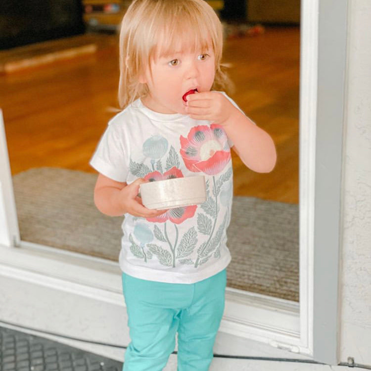 A toddler wearing a white shirt with a floral print eating strawberries