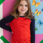 Young girl wearing a navy and red long sleeve tee shirt against a colorful wall