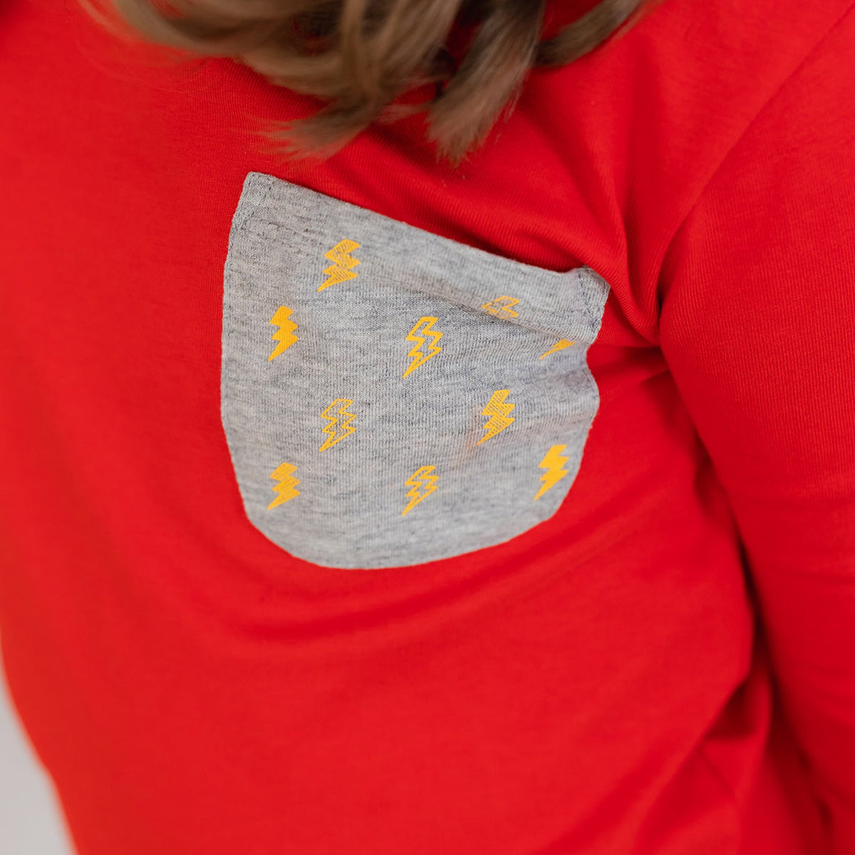 close up view of a gray lightning bolt print pocket on a red shirt