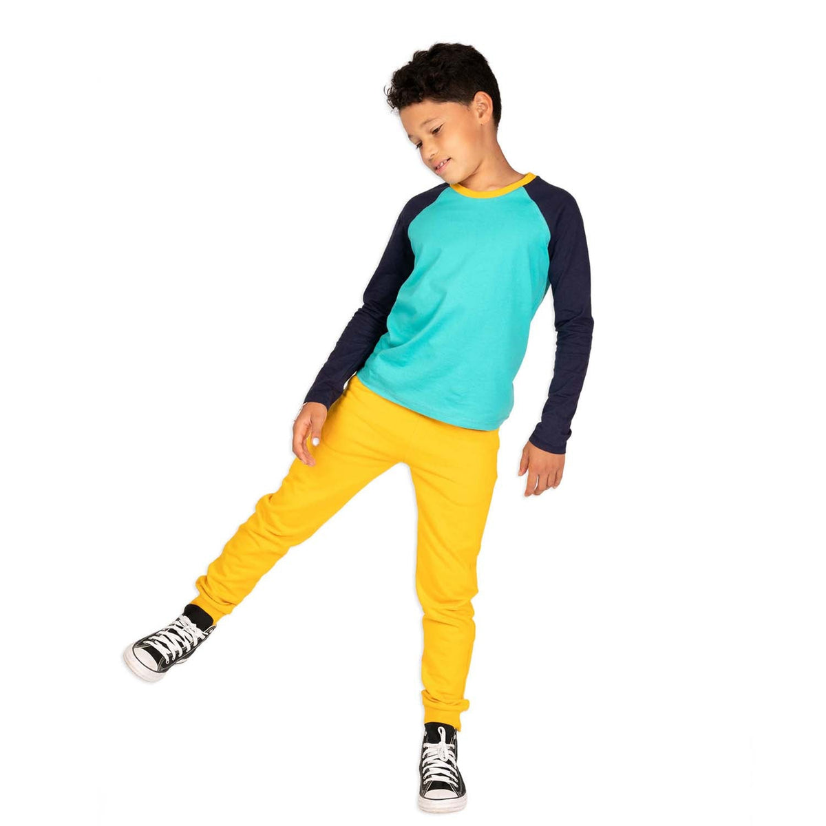 a boy in an active pose wearing a navy and teal long sleeve baseball tee and yellow sweatpants 