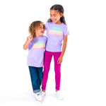 Two children wearing matching purple t-shirts with a rainbow design on a white background