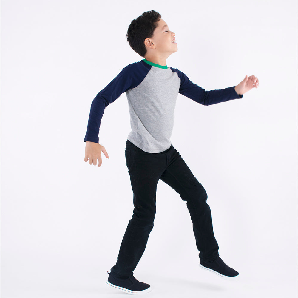 a boy walking wearing a gray and navy blue long sleeve baseball tee and black pants