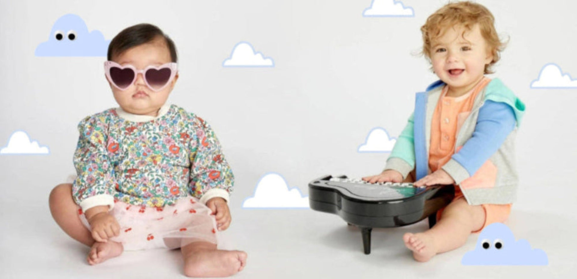 Two children sitting on a white floor with cloud decorations, one wearing sunglasses and a floral outfit, the other playing with a toy.