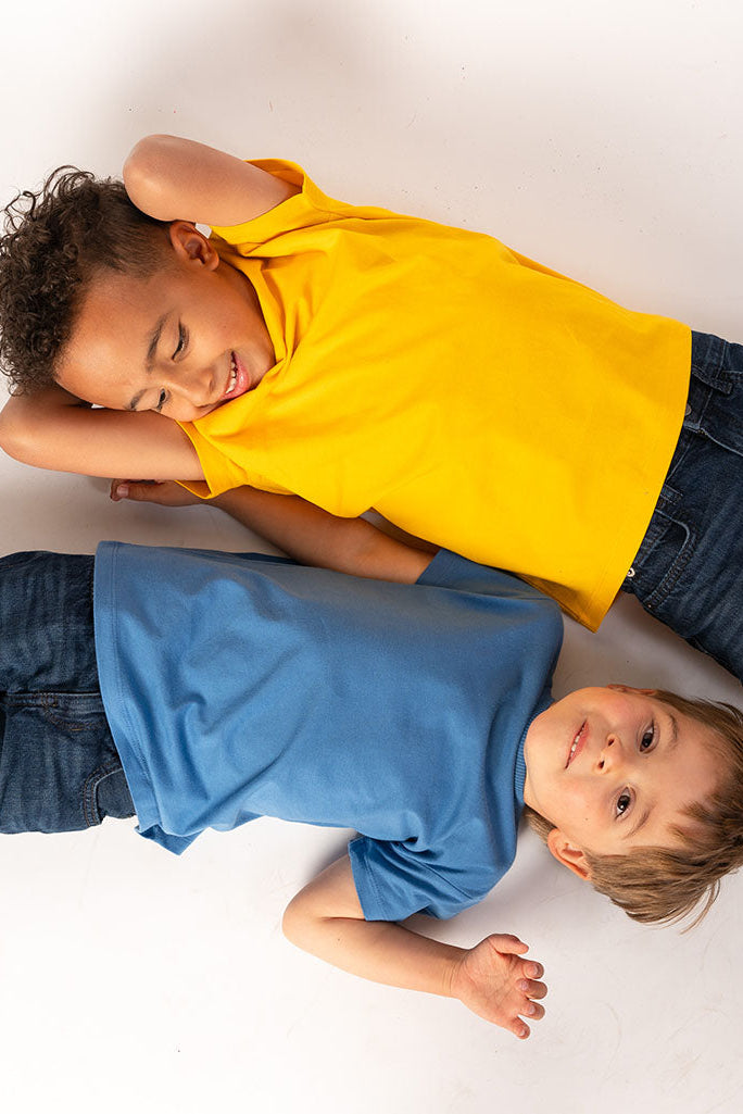 Two children lying on a white floor, one in a yellow shirt and the other in a blue shirt.